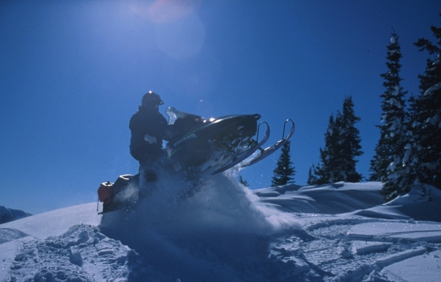 Snowmobile driver jumping snowmobile off the snow